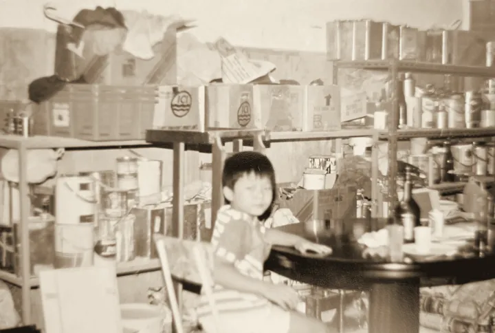 A young boy sitting in the family paint shop, shelves of paint tins behind him