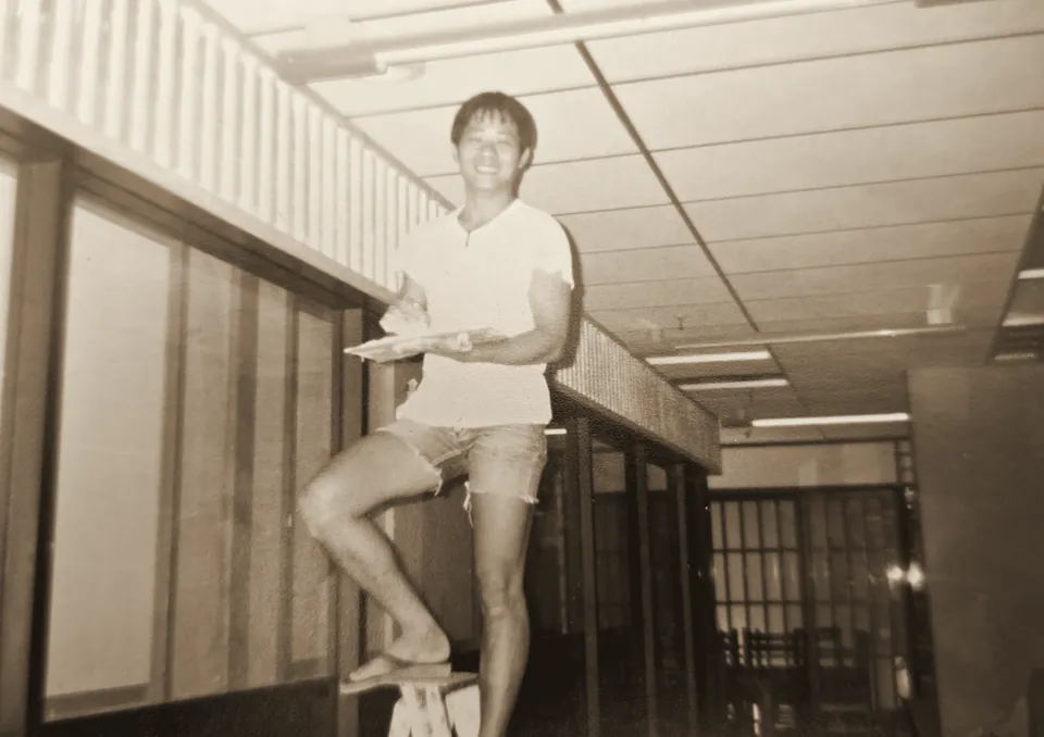Mr Tian Ming on a trestle bench, trowel and hawk in hand, smiling at the camera